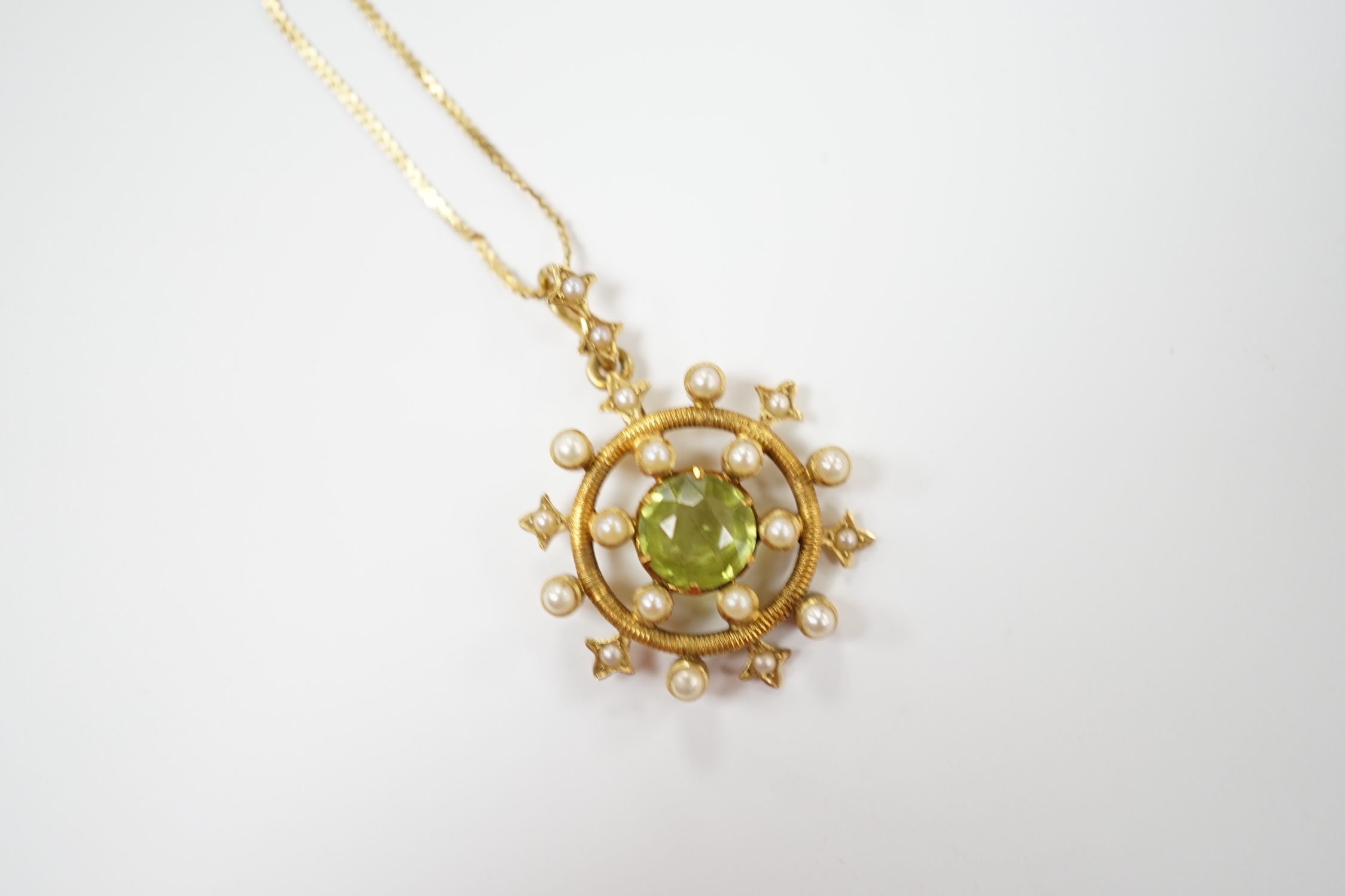 An Edwardian yellow metal, peridot and seed pearl cluster set 'wheel' pendant, overall 30mm, on a later 14k chain, gross weight 5.2 grams.